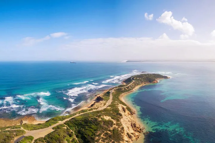 Vista aérea de una carretera costera que se extiende por una verde península junto al mar.