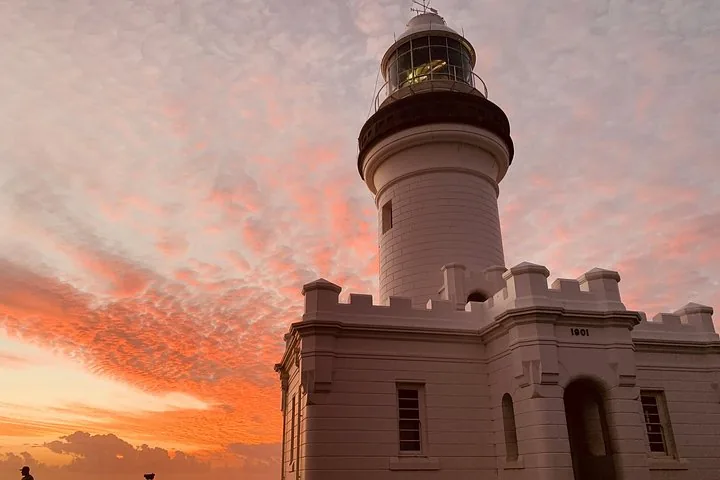 Un phare blanc se dressant fièrement sur fond de ciel de coucher de soleil orange spectaculaire.