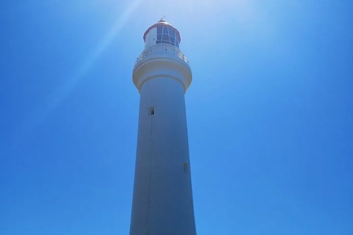 Blick nach oben zu einem hohen, weißen Leuchtturm vor einem klaren, blauen Himmel.